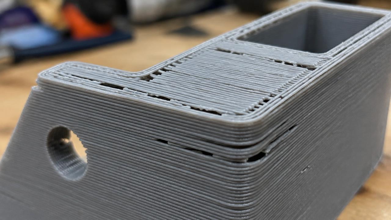 Close-up of a gray 3D printed part showing gaps between extrusion lines and an incomplete top layer caused by under-extrusion